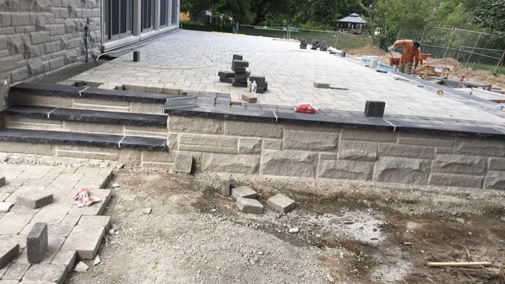 Engineered-block retaining wall under construction, holding back the grade beneath a paver surface