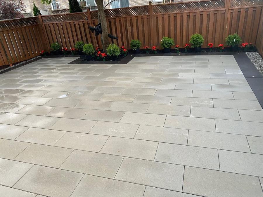 Large grey slab patio in a fenced backyard with a planted border