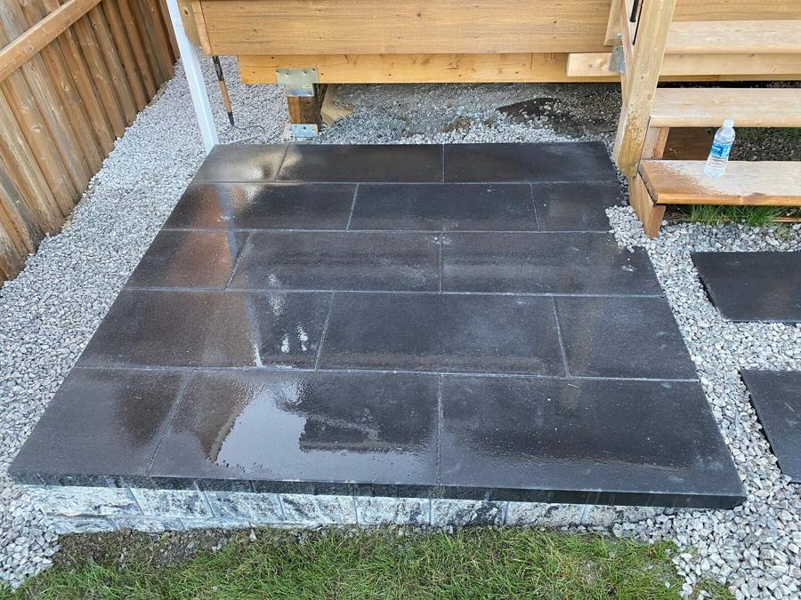Dark granite-tone slab patio with a gravel border and cedar deck