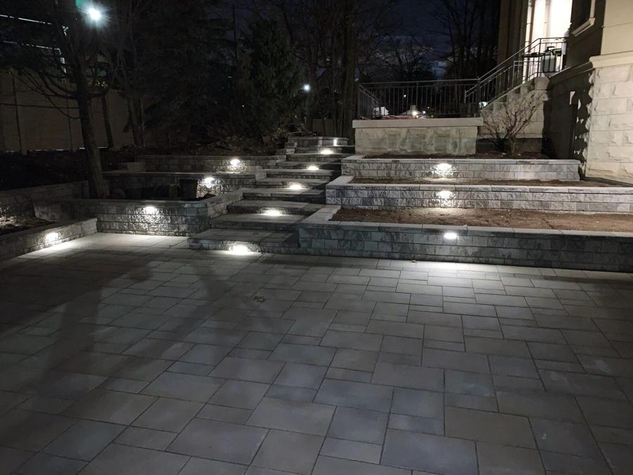 Backyard interlock patio lit at dusk with landscape lighting and steps