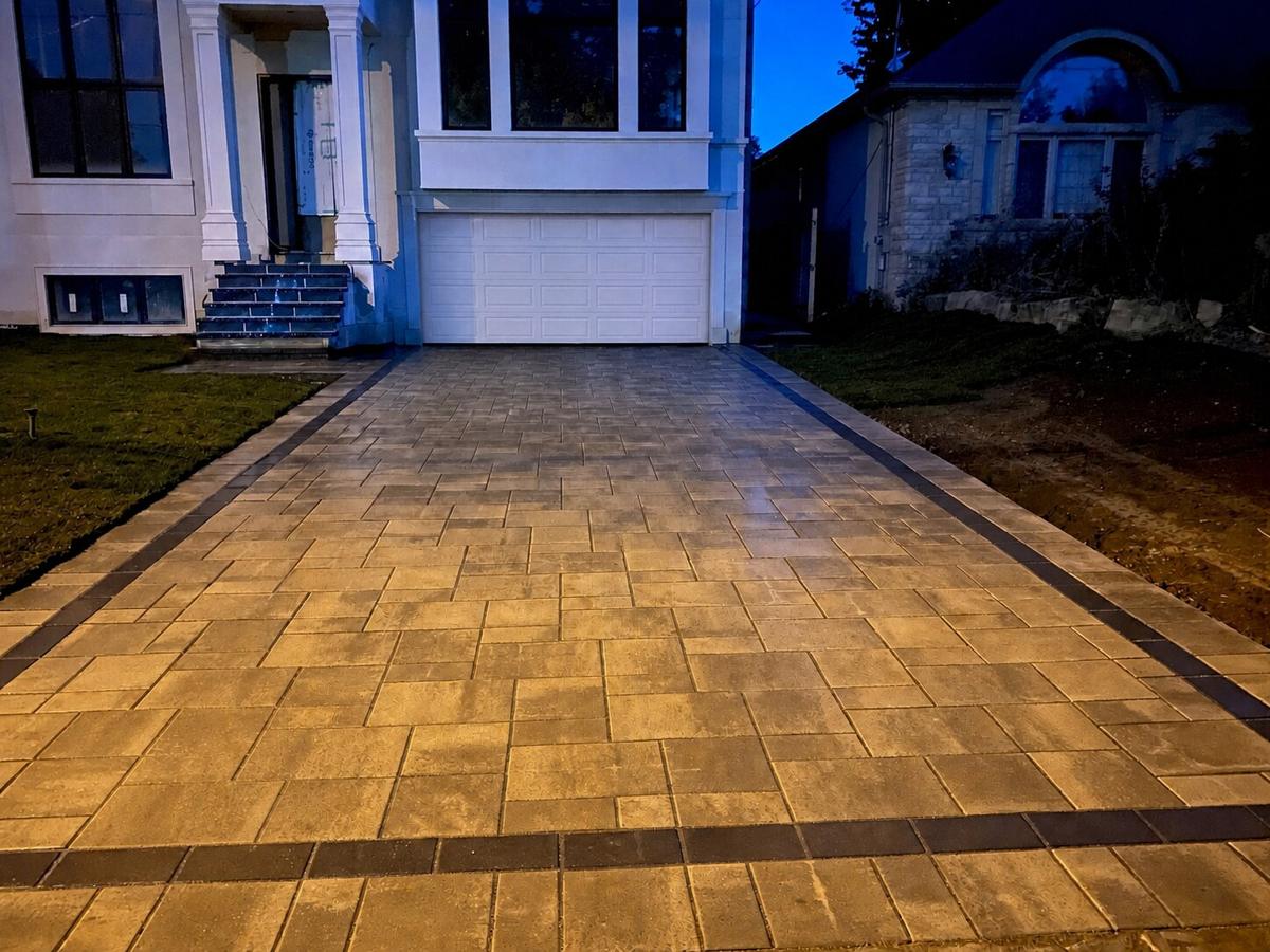 Warm-toned interlock driveway lit at dusk in front of a home