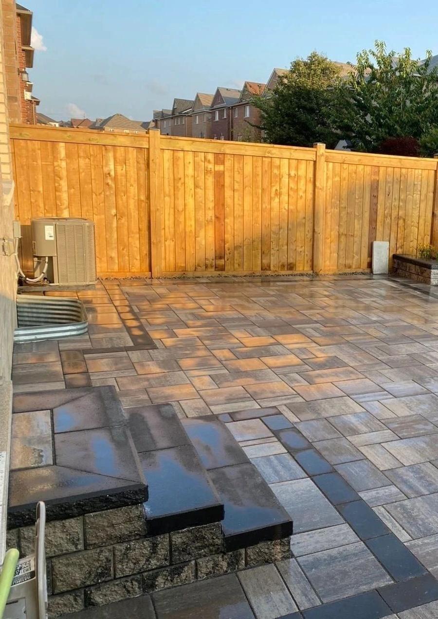 Interlock patio with a dark border beside a wood fence