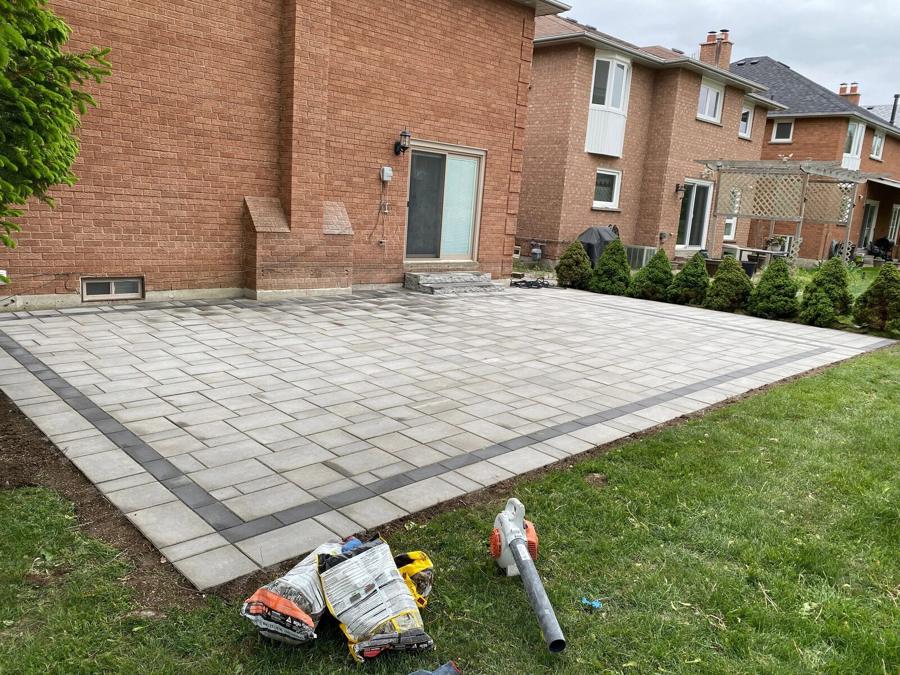 Wide backyard patio in banded pavers laid against the back of a brick home