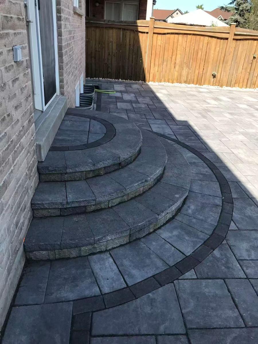 Curved paver steps with a charcoal band sweeping down to a patio beside a brick house