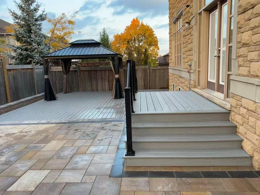 Grey deck with a hardtop gazebo and broad entrance steps beside a paver patio