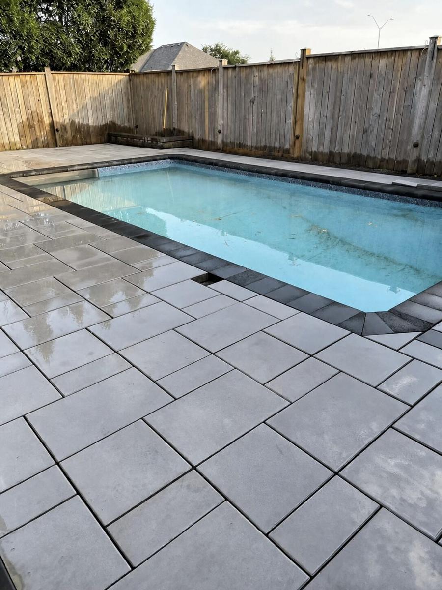 Rectangular pool surrounded by large-format grey slab paving against a weathered wood fence