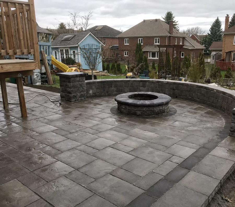 Curved paver patio with a round stone fire pit set inside a matching curved seat wall