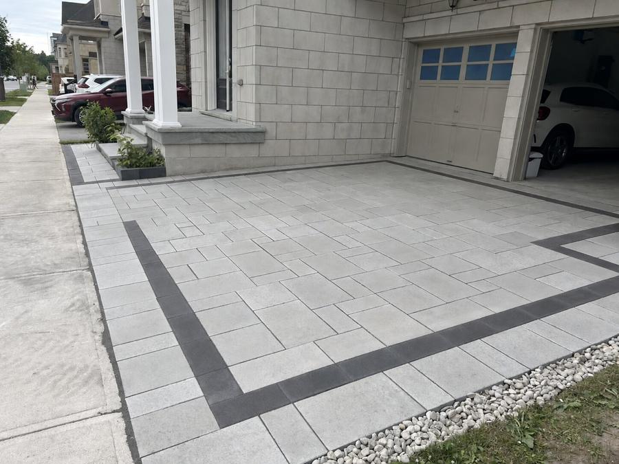 Grey interlock driveway with charcoal borders and pebble edging running to steps at a columned porch