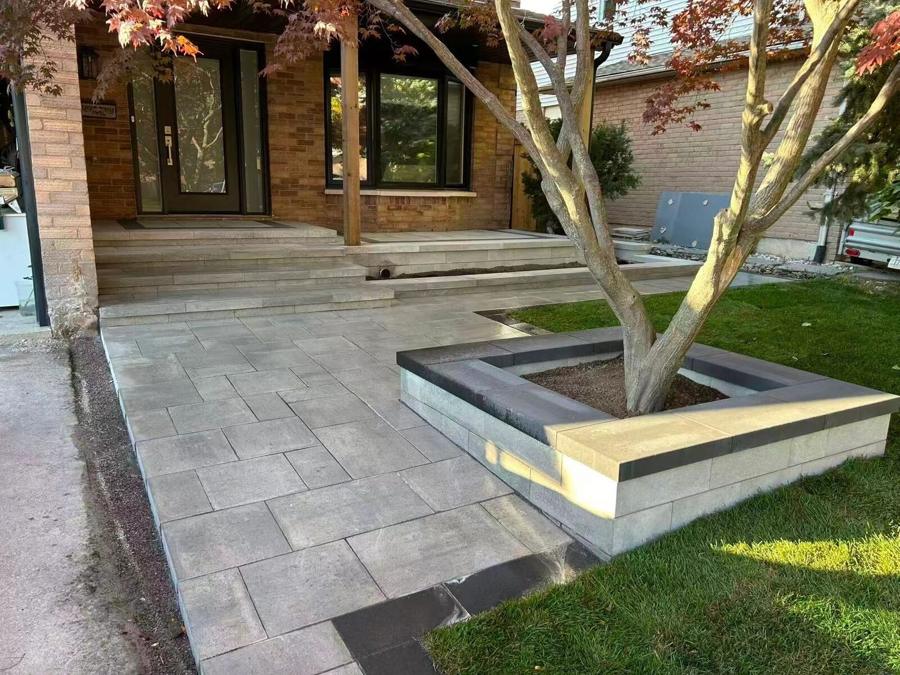 Raised natural-stone planter around a tree beside a paver walkway and fresh lawn