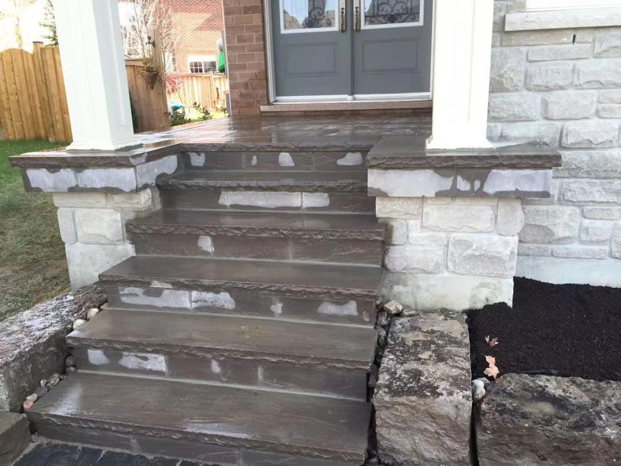 Stone entrance steps under construction between stone-clad porch columns