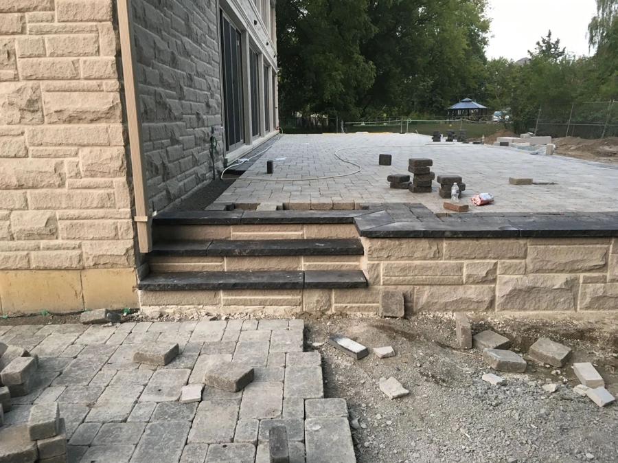 Block retaining wall and inset steps supporting a raised paver patio under construction