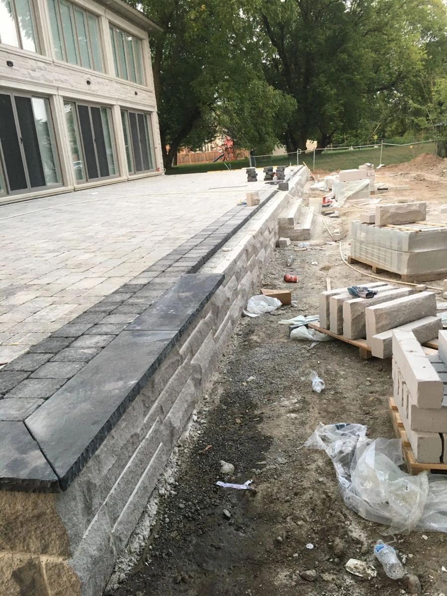 Segmental-block retaining wall with dark coping beside a raised patio under construction