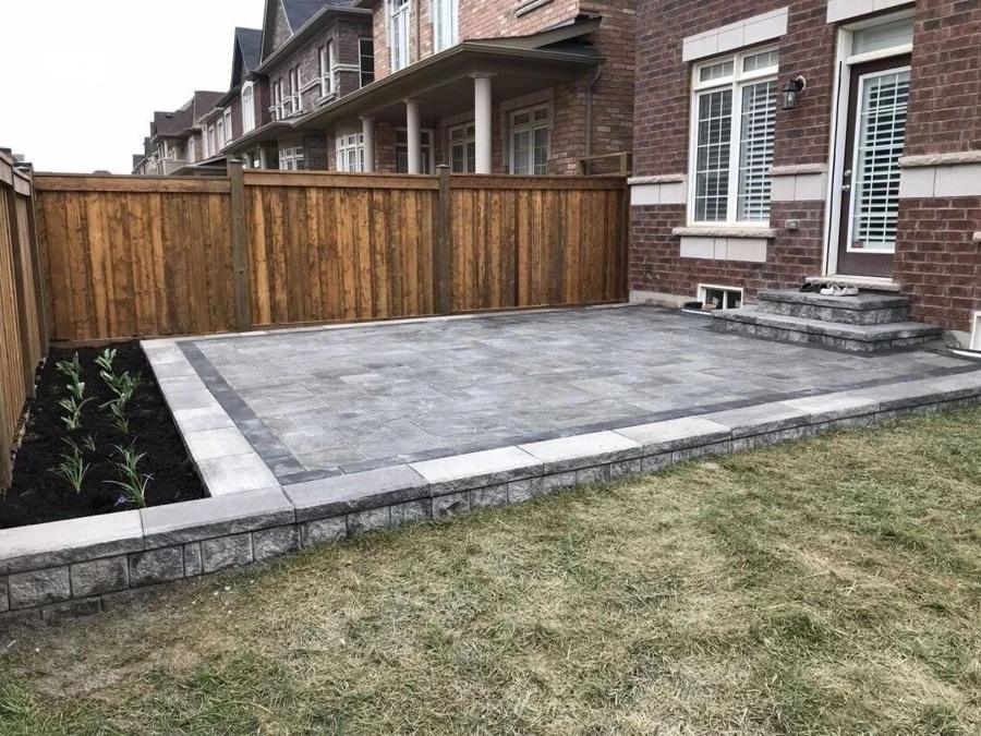 Interlock patio bordered by a wood privacy fence and a raised bed