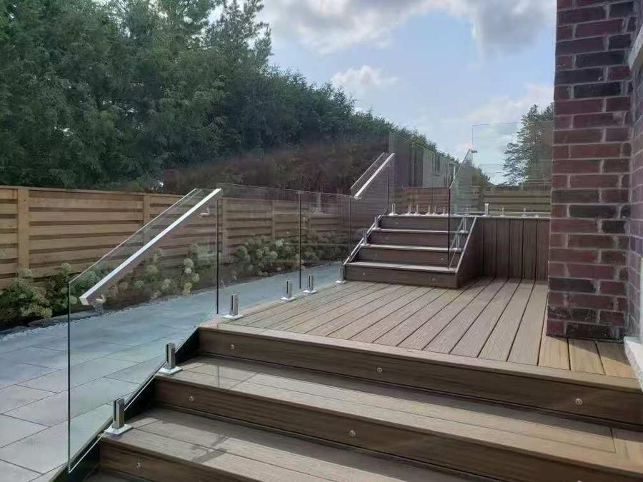 Composite deck with glass railings and steps beside a planted border