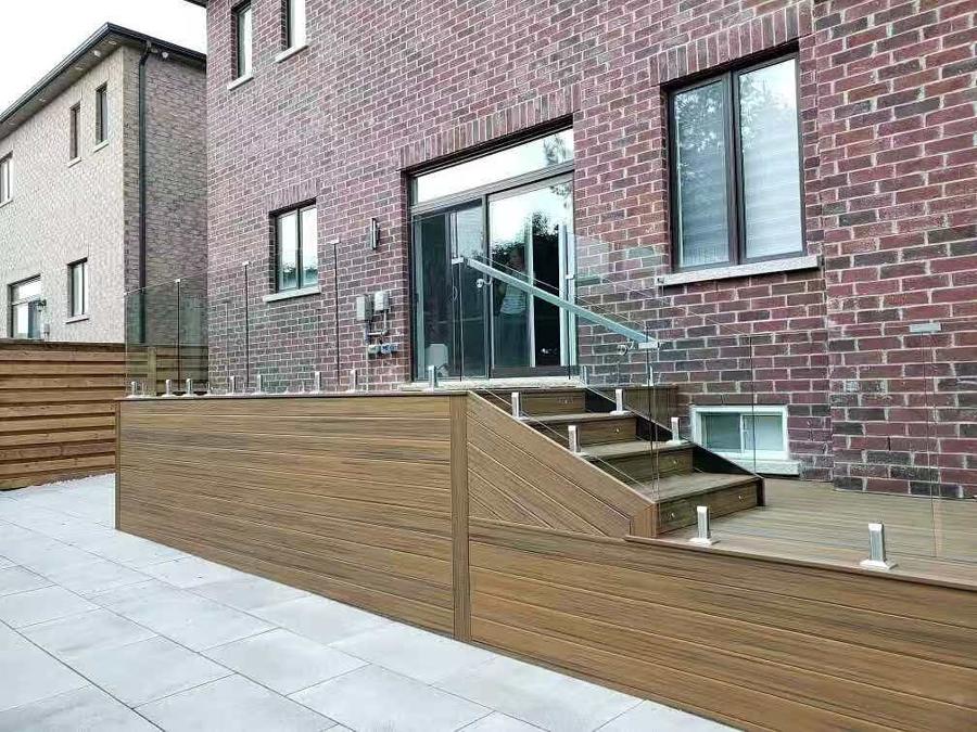 Raised deck with glass railings, horizontal board skirting and steps above a slab patio