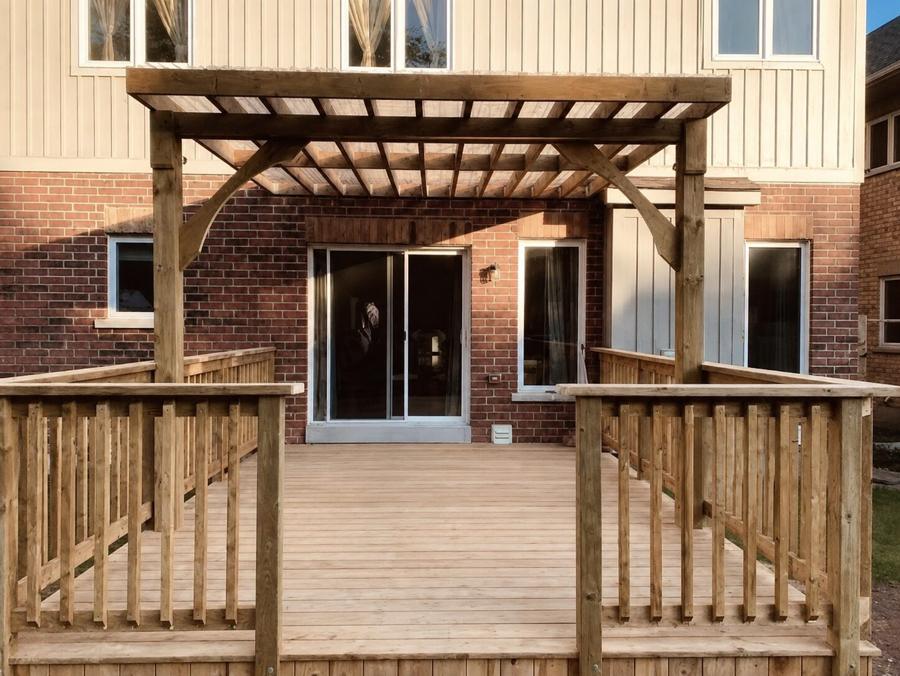 Cedar pergola over a raised deck with a spindle railing, against a brick and board-and-batten house