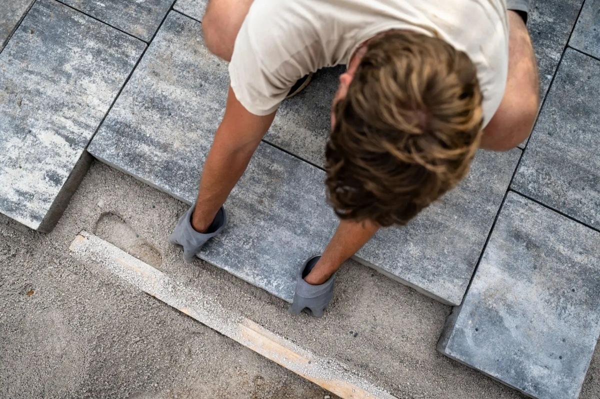 Overhead view of an installer carefully setting large-format grey slab pavers with joint spacers on a prepared base.