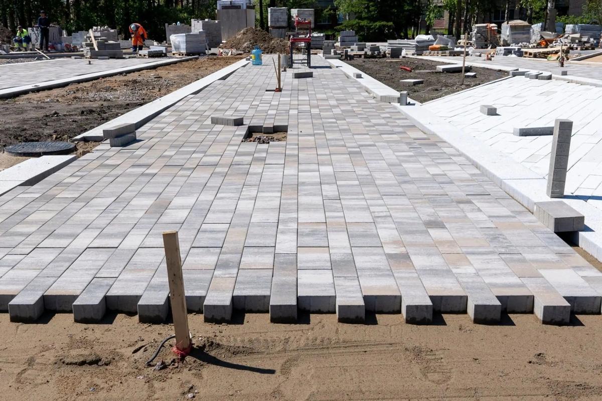 A wide interlock walkway being laid with smooth grey pavers on a levelled sand base, more pavers stacked in the background.
